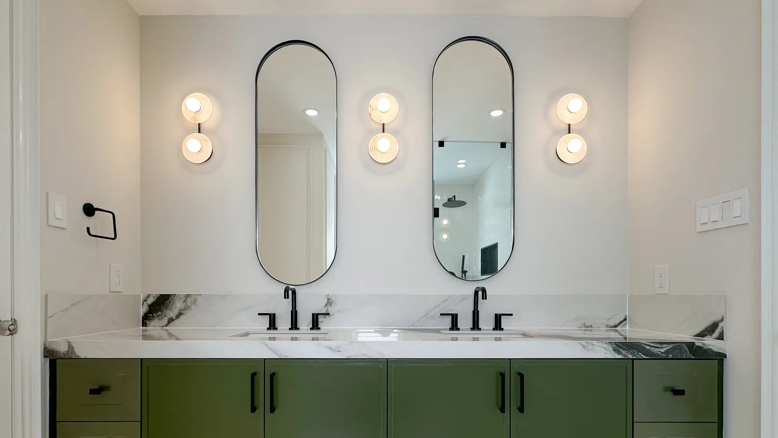 A finished bathroom renovation with a green double vanity, marble countertop, oval mirrors, and black fixtures — the kind of job whose real profit depends on tracking every expense
